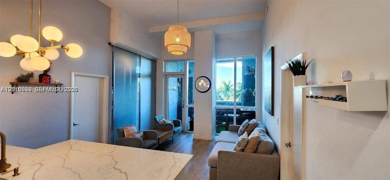 244 Biscayne Boulevard, #301, Miami, FL 33132 High-ceiling interior featuring a gold-finish multi-globe chandelier, a woven pendant light, expansive floor-to-ceiling windows, and a countertop with stone-patterned surfacing