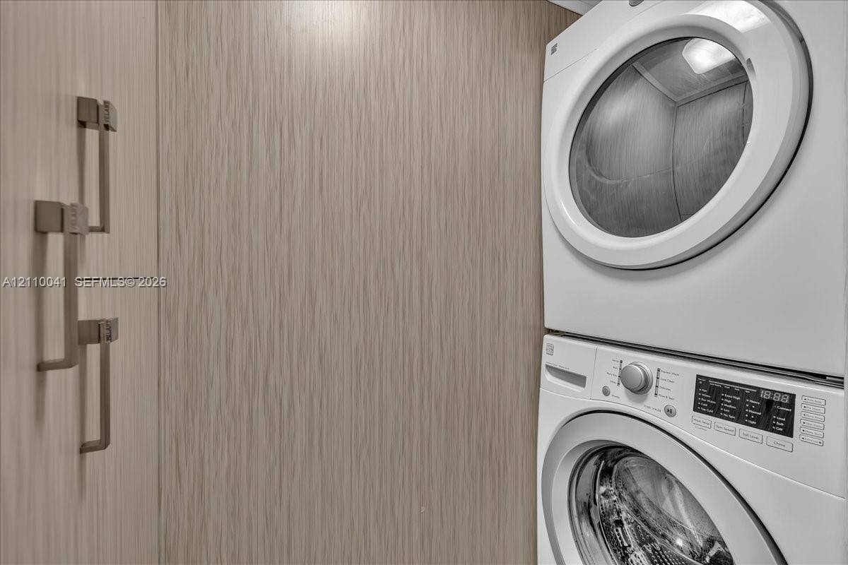 1610 Lenox Avenue, #516, Miami Beach, FL 33139 Stacked washer and dryer unit featuring built-in cabinetry with metallic bar hardware and a light-toned wood-finish exterior