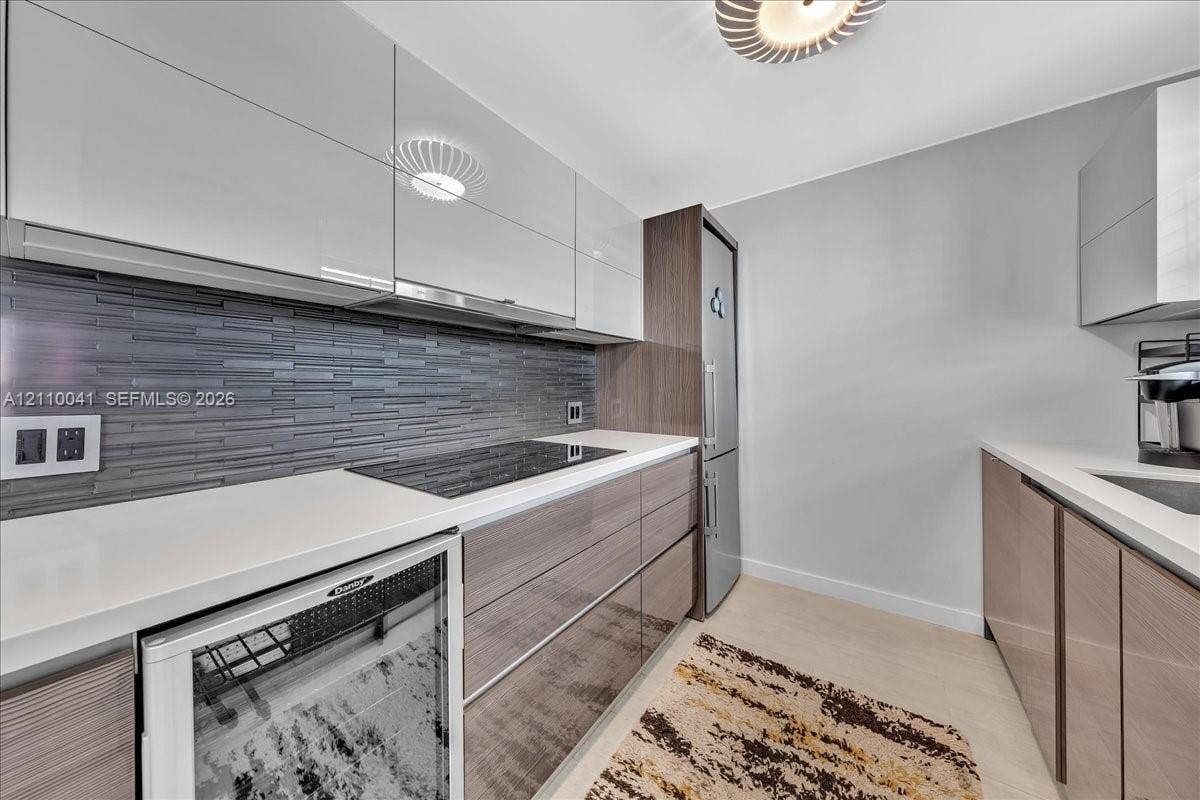 1610 Lenox Avenue, #516, Miami Beach, FL 33139 Modern kitchen featuring high-gloss cabinetry, linear tile backsplash, solid-surface countertops, integrated cooktop, and built-in beverage refrigerator