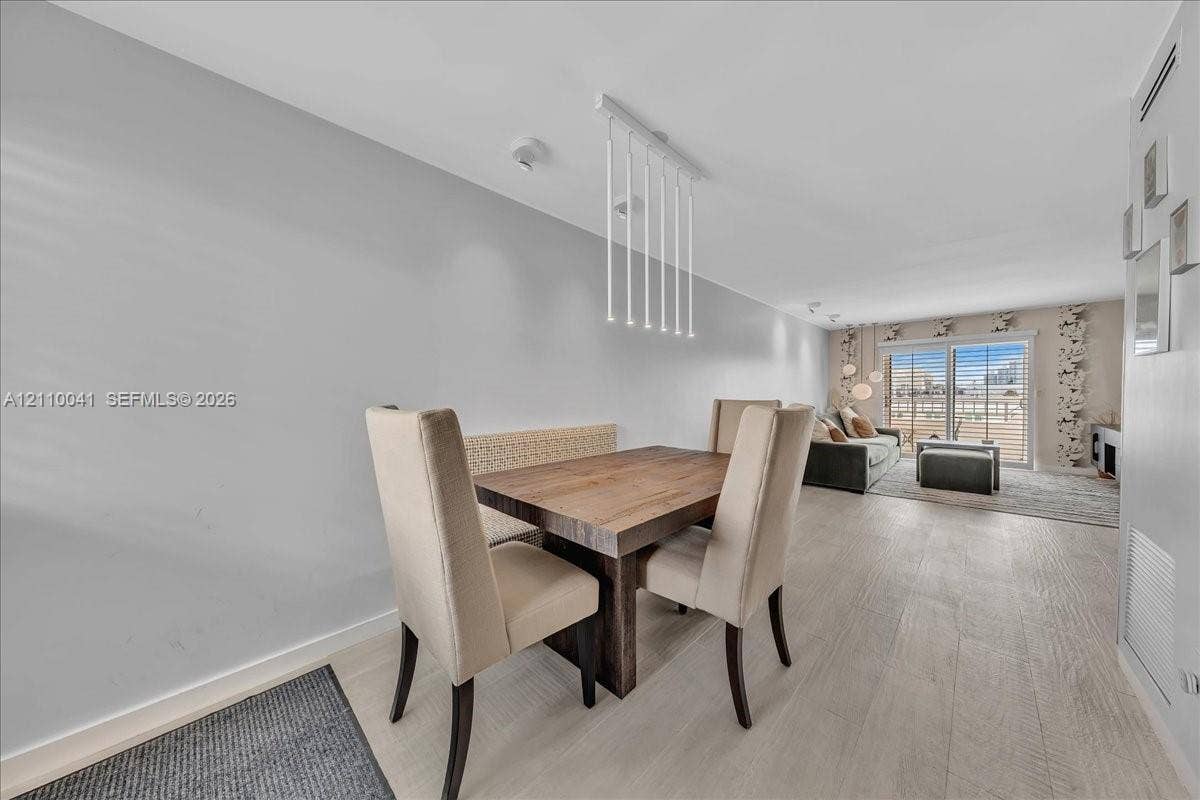 1610 Lenox Avenue, #516, Miami Beach, FL 33139 Open floor plan featuring wood-finish flooring, a contemporary linear pendant light fixture, and sliding glass doors with direct access to an exterior deck