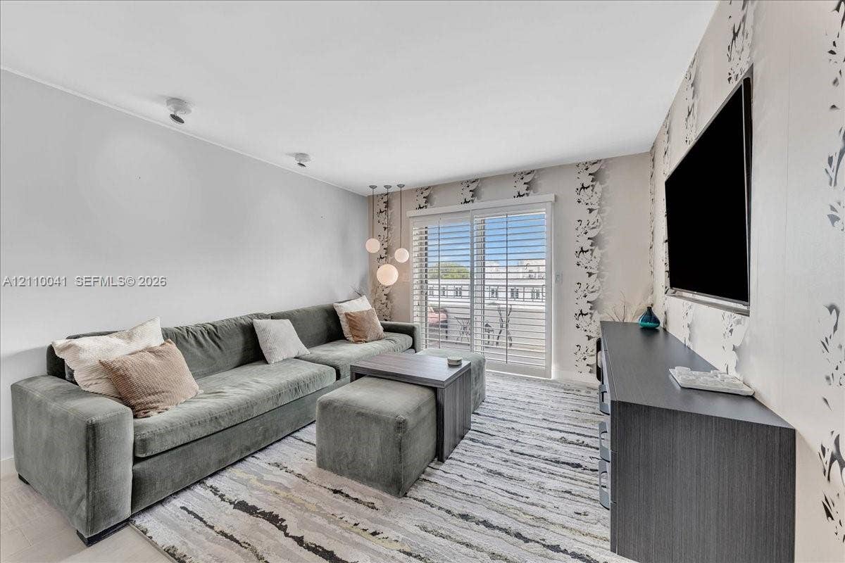 1610 Lenox Avenue, #516, Miami Beach, FL 33139 Living area featuring glass sliding doors with plantation shutters, recessed ceiling lighting, three-globe pendant lighting, and an accent wall with patterned wall covering
