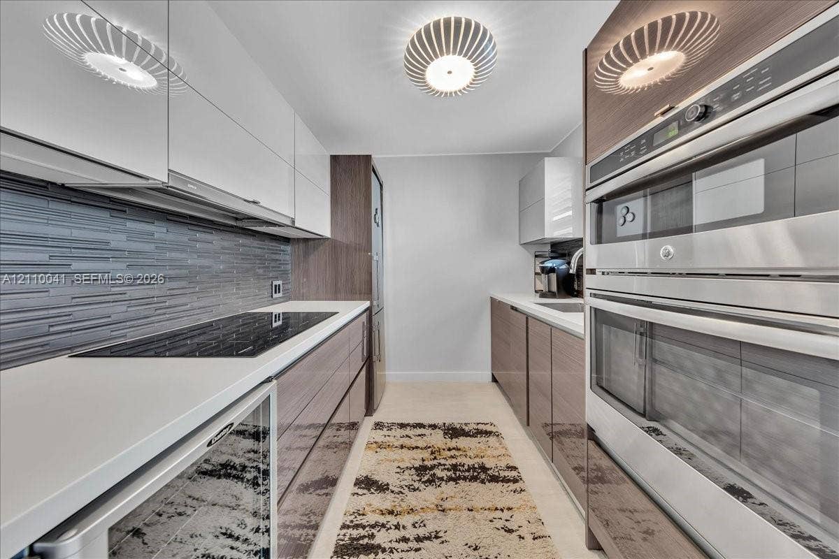 1610 Lenox Avenue, #516, Miami Beach, FL 33139 Contemporary kitchen featuring high-gloss cabinetry, stainless steel double wall ovens, a glass cooktop, stone-finish countertops, and a textured tile backsplash