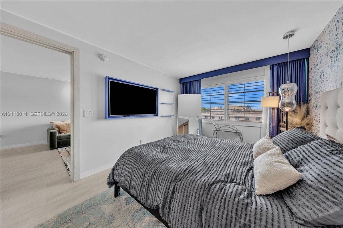 1610 Lenox Avenue, #516, Miami Beach, FL 33139 Bedroom featuring wood-finish flooring, multi-pane window, built-in television mount, decorative accent wall, and pendant lighting
