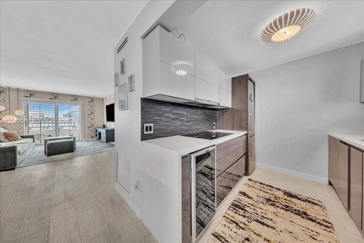 1610 Lenox Avenue, #516, Miami Beach, FL 33139 Kitchen featuring high-gloss cabinetry, stone-surface countertops, a textured tile backsplash, integrated glass-door beverage chiller, and a sculptural flush-mount ceiling fixture