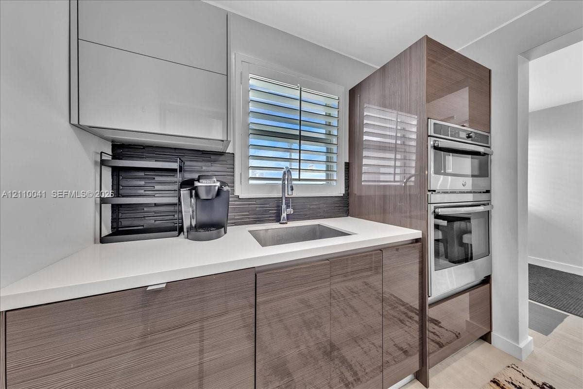 1610 Lenox Avenue, #516, Miami Beach, FL 33139 High-gloss cabinetry, stone-finish countertops, stainless steel dual wall oven, dark linear tile backsplash, and undermount stainless steel sink