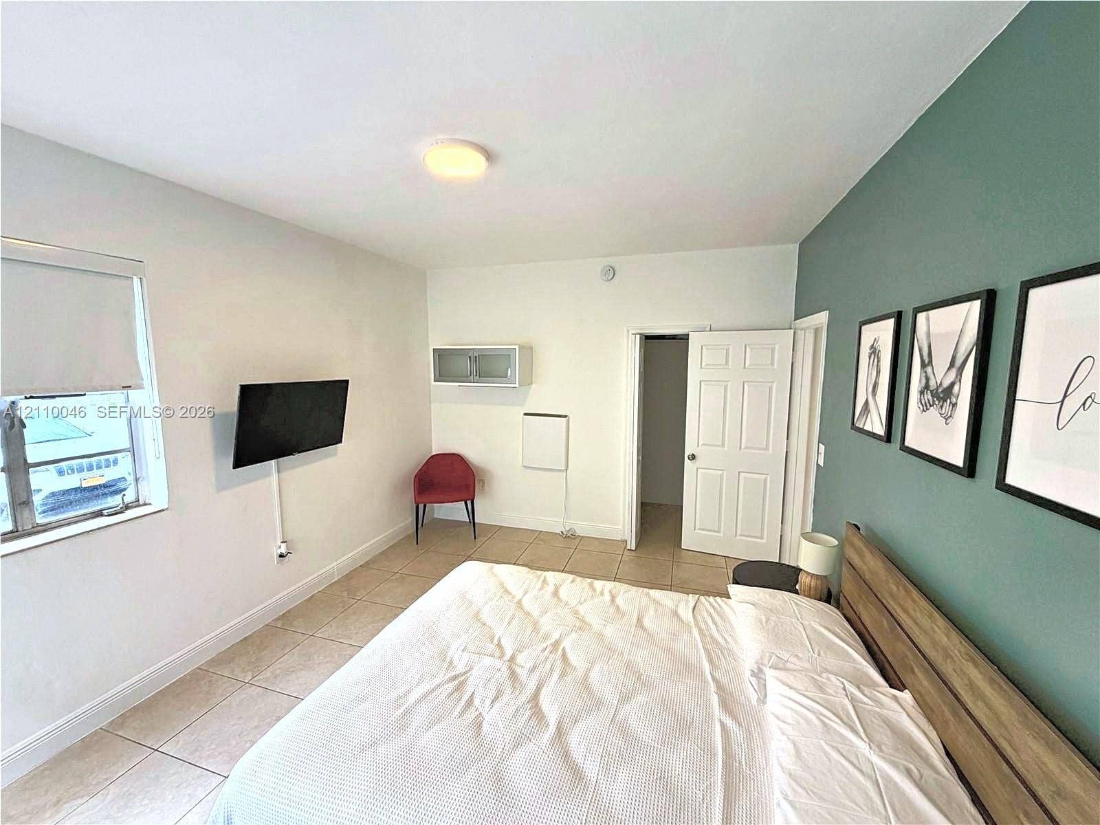 Room featuring ceramic tile flooring, a dual-tone wall design with an accent wall, a built-in overhead storage cabinet, and a six-panel interior door