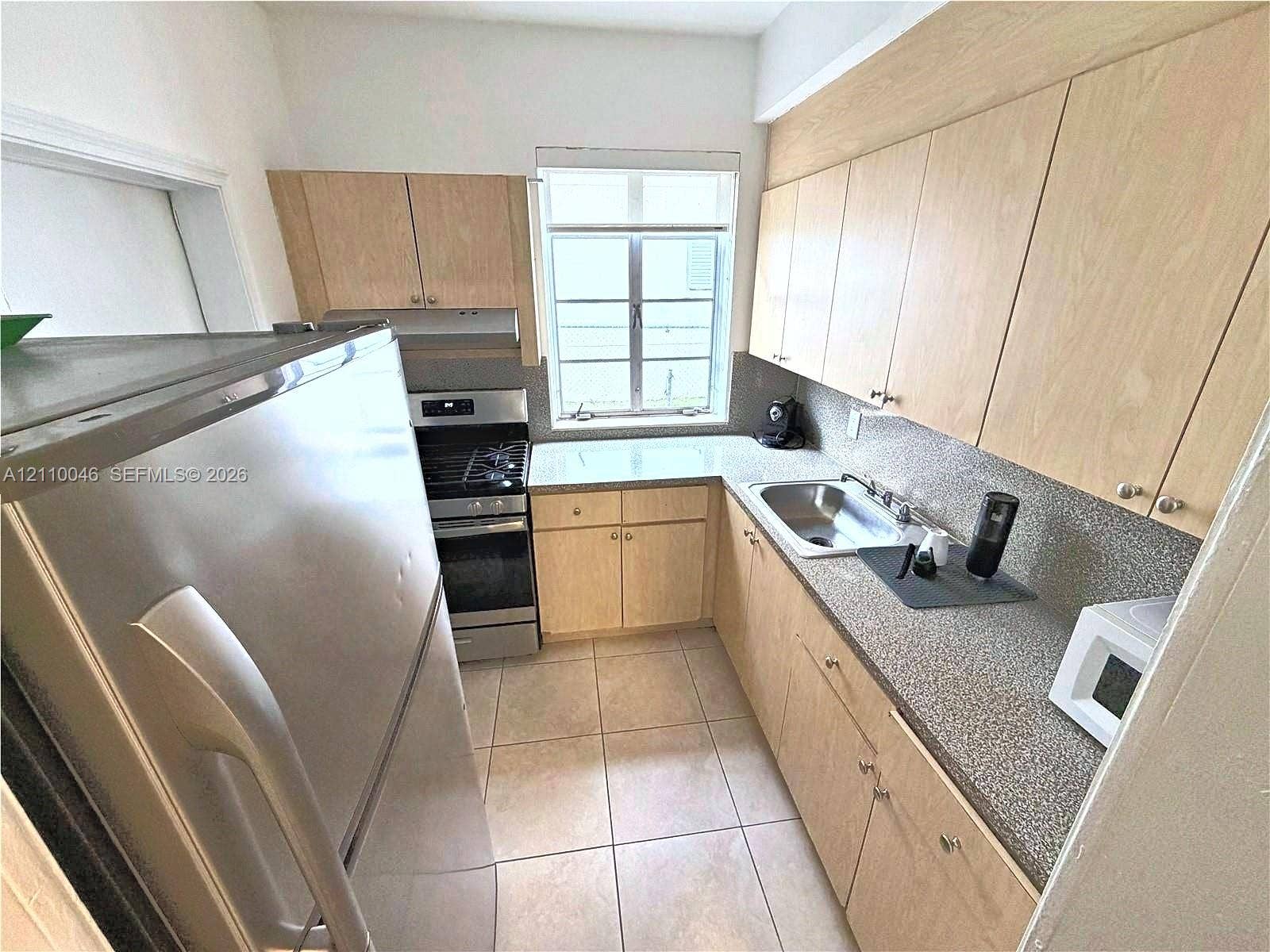 Kitchen featuring light wood-finish cabinetry, solid surface countertops, stainless steel appliances, a double-basin sink, and ceramic tile flooring