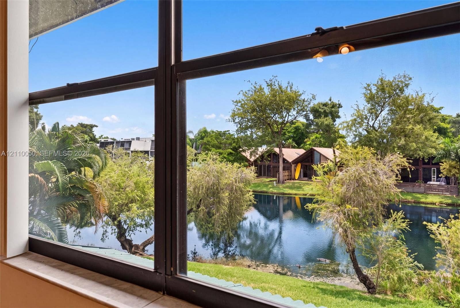 506 Westree Lane, Plantation, Plantation, FL 33324 Large window featuring a metal frame and a stone-finish sill, showcasing exterior scenery including a pond, manicured landscaping, and mature trees