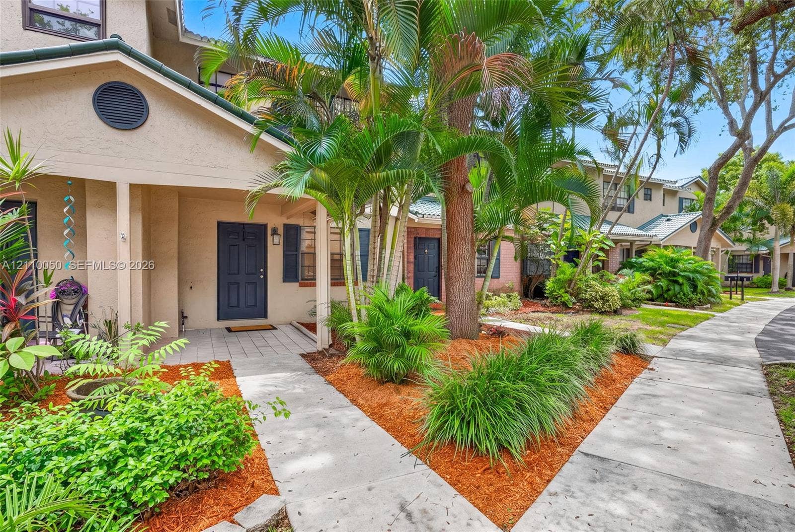 506 Westree Lane, Plantation, Plantation, FL 33324 Exterior facade featuring a stucco finish, covered entryway, panel-style front door, paved walkway, and mature tropical landscaping