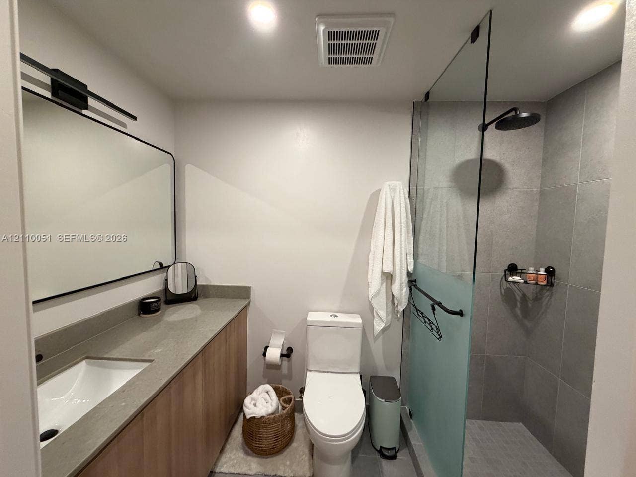 121 NE 5th Street, #1703, Miami, FL 33132 Bathroom featuring a wood-finish vanity with a stone-surface countertop, a frameless glass-enclosed shower with large-format tile surround, and matte black plumbing fixtures