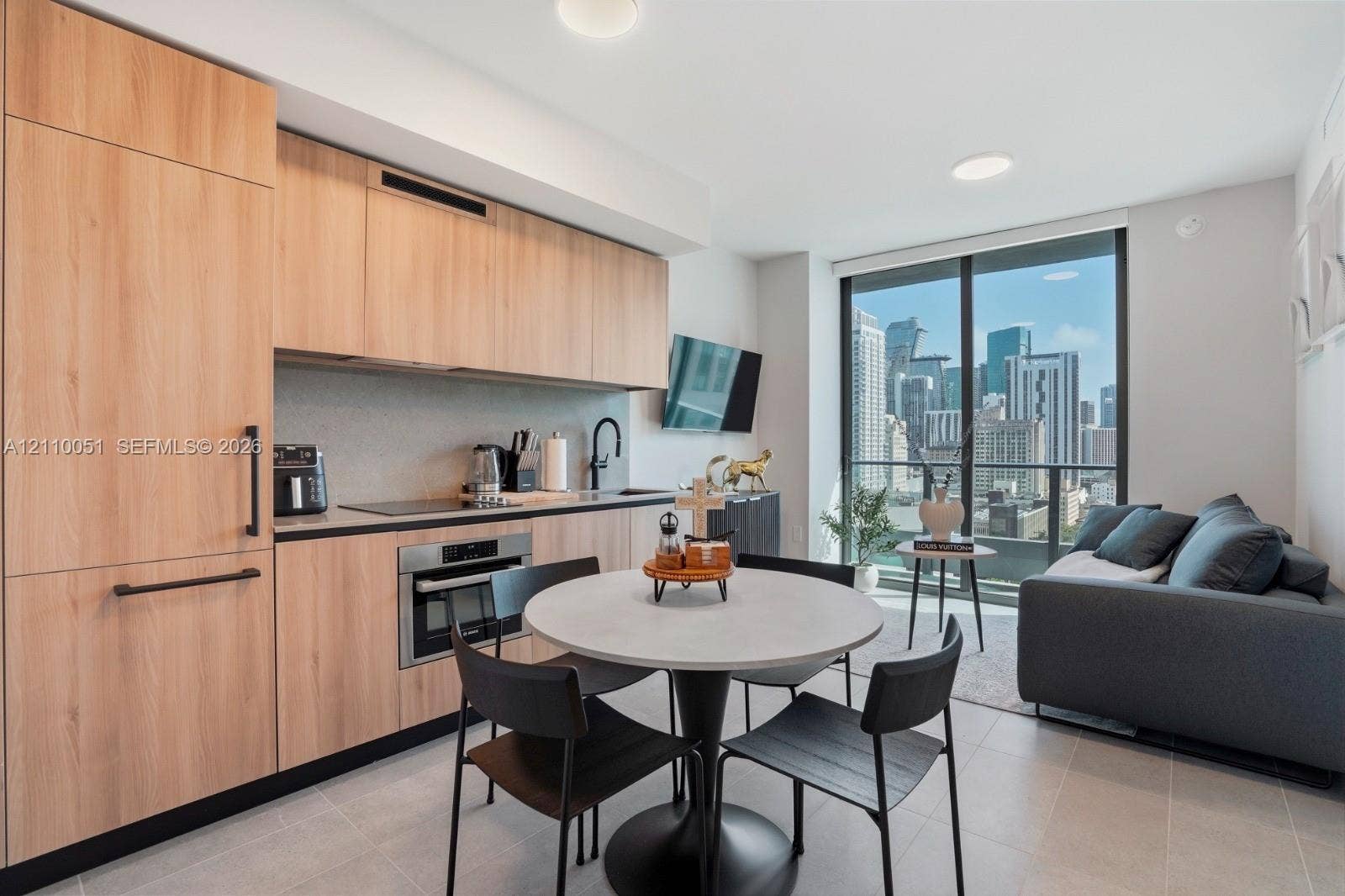 121 NE 5th Street, #1703, Miami, FL 33132 Kitchen featuring custom light-toned cabinetry, built-in panel-ready appliances, quartz countertops, and floor-to-ceiling glass sliding doors with an urban skyline backdrop