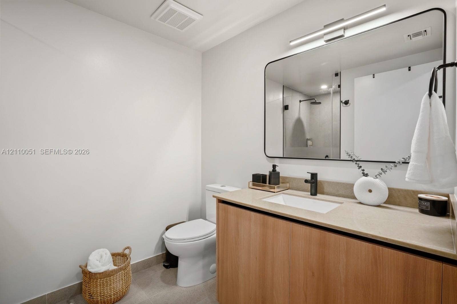121 NE 5th Street, #1703, Miami, FL 33132 Wood-finish vanity cabinet with a stone-surface countertop, rectangular undermount sink, matte black faucet, and large rectangular mirror with rounded edges