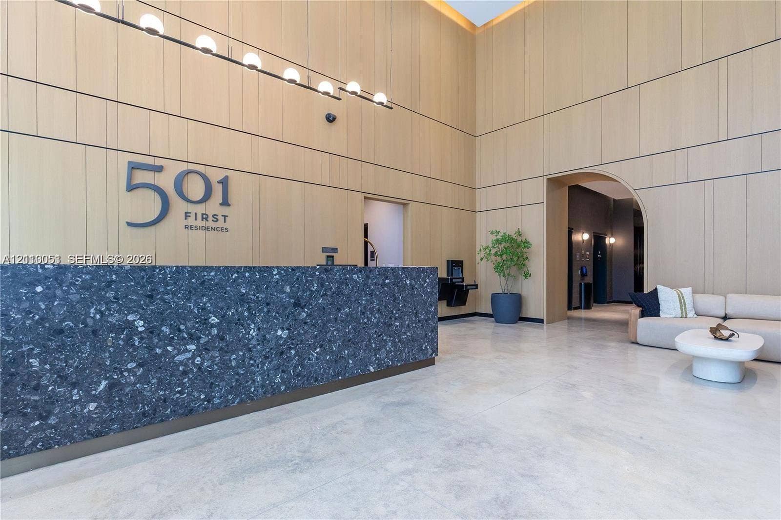 121 NE 5th Street, #1703, Miami, FL 33132 Lobby featuring double-height ceilings, wood-paneled walls, polished concrete flooring, a dark aggregate reception desk, and linear pendant lighting