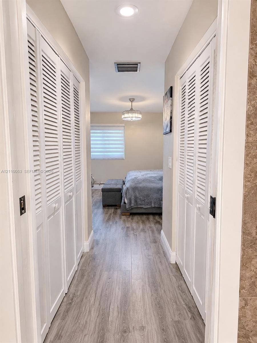 Hallway featuring wood-finish flooring, dual sets of white louvered-door closets, and recessed lighting