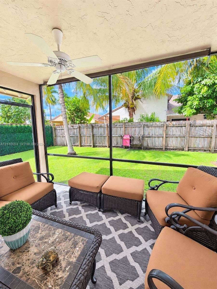 Screened lanai featuring a ceiling-mounted fan and tile flooring, providing an enclosure for the expansive backyard with a manicured lawn and wood-panel fencing