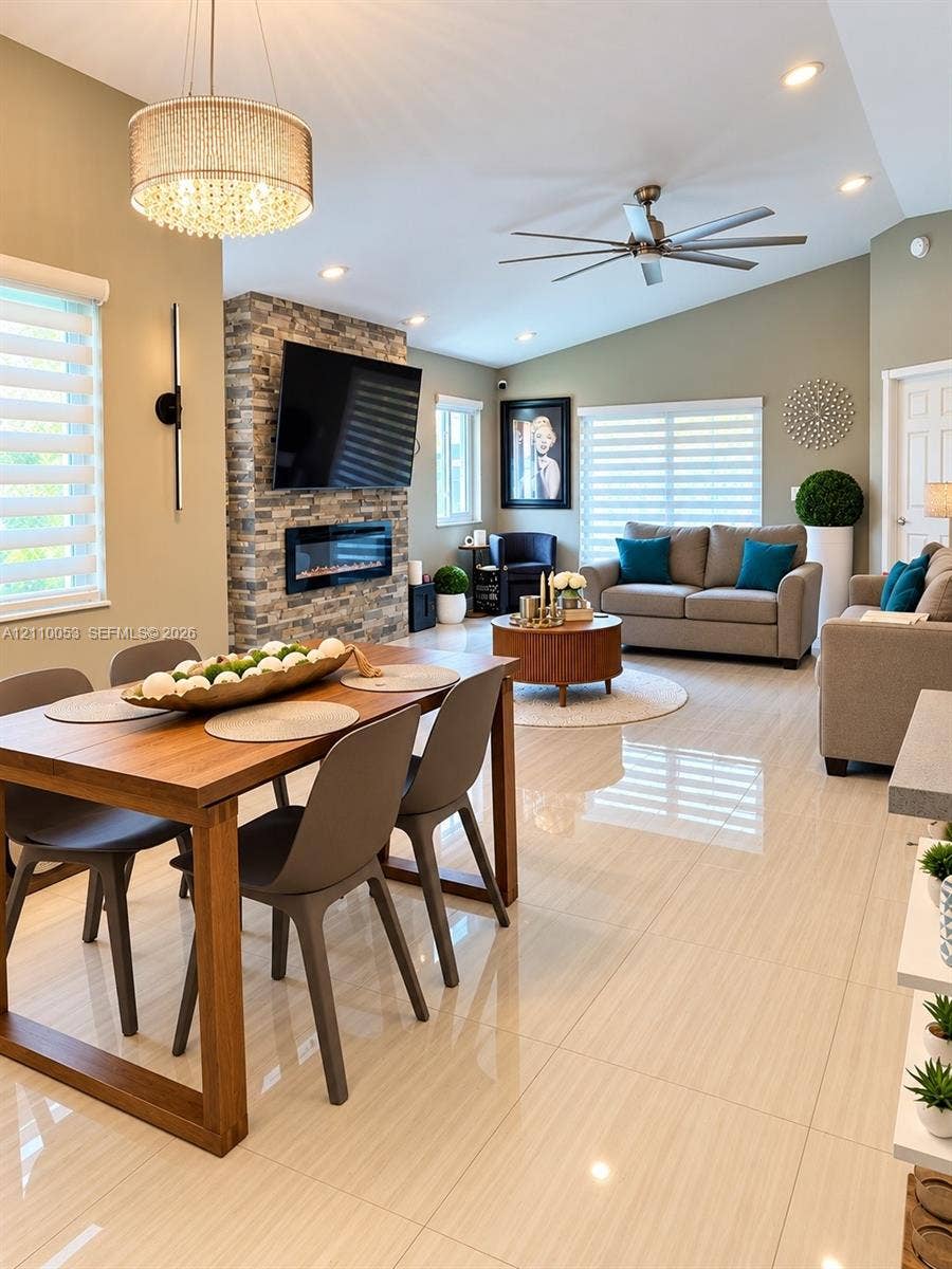 Open-concept living space featuring high vaulted ceilings, large-format polished tile flooring, a floor-to-ceiling stone fireplace surround with integrated electric hearth, and a contemporary multi-tier drum chandelier
