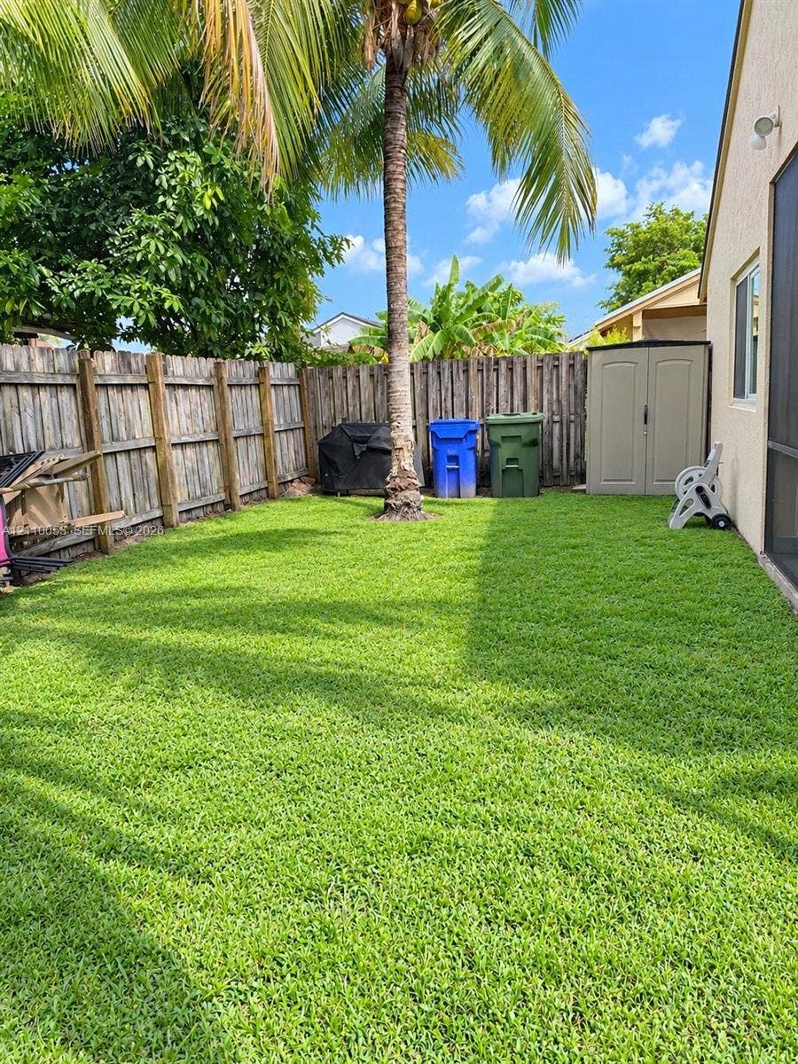 Private backyard featuring a manicured lawn, wood-panel fencing, and a mature palm tree
