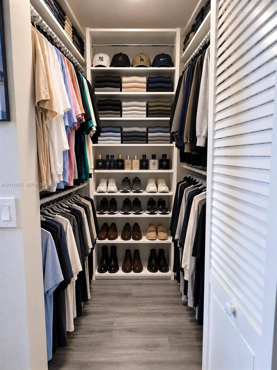 Walk-in closet featuring custom white built-in shelving, multi-level hanging rods, and wood-finish flooring