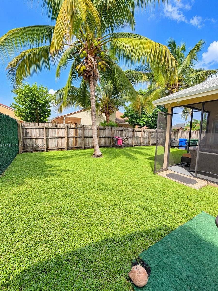 Private backyard featuring a manicured lawn, perimeter wood fencing, a mature palm tree, and a screened-in lanai