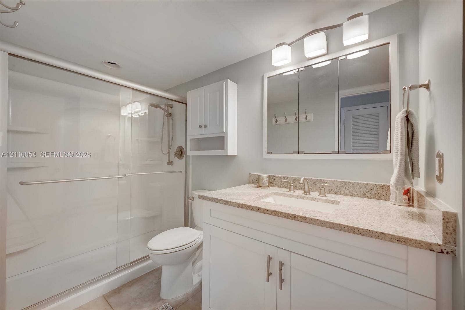 Bathroom featuring a stone-top vanity with an undermount sink, a three-light fixture, a recessed medicine cabinet, and a walk-in shower with glass sliding doors