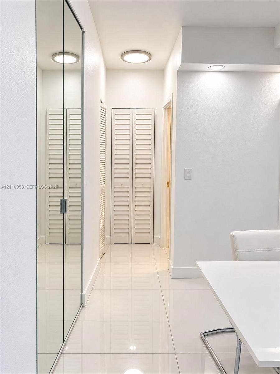 1950 S Ocean Drive, #3K, Hallandale Beach, Hallandale Beach, FL 33009 Hallway featuring floor-to-ceiling mirrored sliding closet doors, white louvered bifold closet doors, high-gloss tile flooring, and flush-mount ceiling lighting