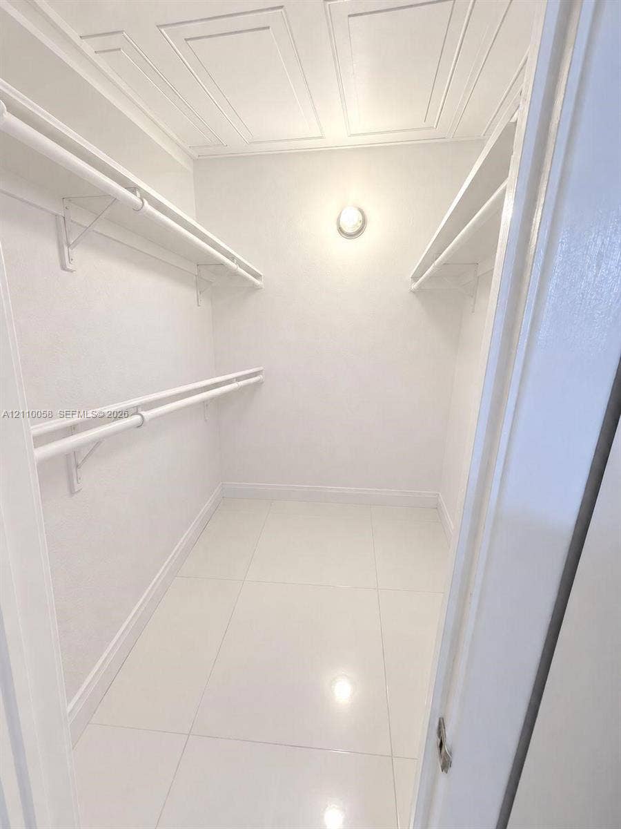 1950 S Ocean Drive, #3K, Hallandale Beach, Hallandale Beach, FL 33009 Walk-in closet featuring large-format tile flooring, multi-level wall-mounted shelving and hanging rods, ceiling molding, and a fixed circular wall-mounted light fixture