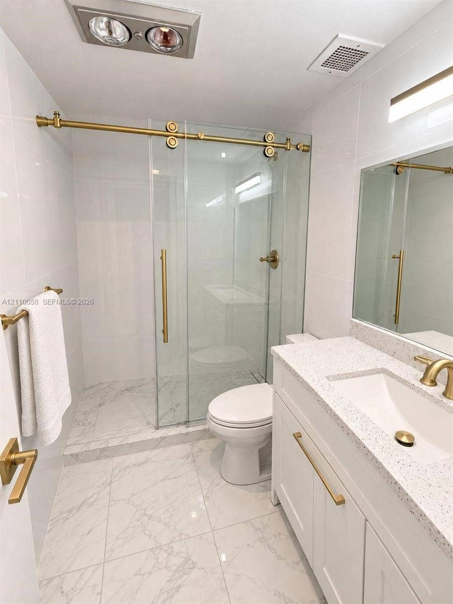 1950 S Ocean Drive, #3K, Hallandale Beach, Hallandale Beach, FL 33009 Bathroom featuring a walk-in shower with a glass sliding door, brass hardware, stone-finish tile flooring, quartz-surface vanity countertop, and white shaker-style cabinetry