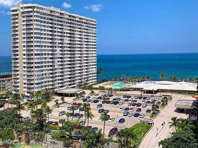 1950 S Ocean Drive, #3K, Hallandale Beach, Hallandale Beach, FL 33009 High-rise residential building featuring private balconies, surface parking, an outdoor swimming pool, and tropical landscaping