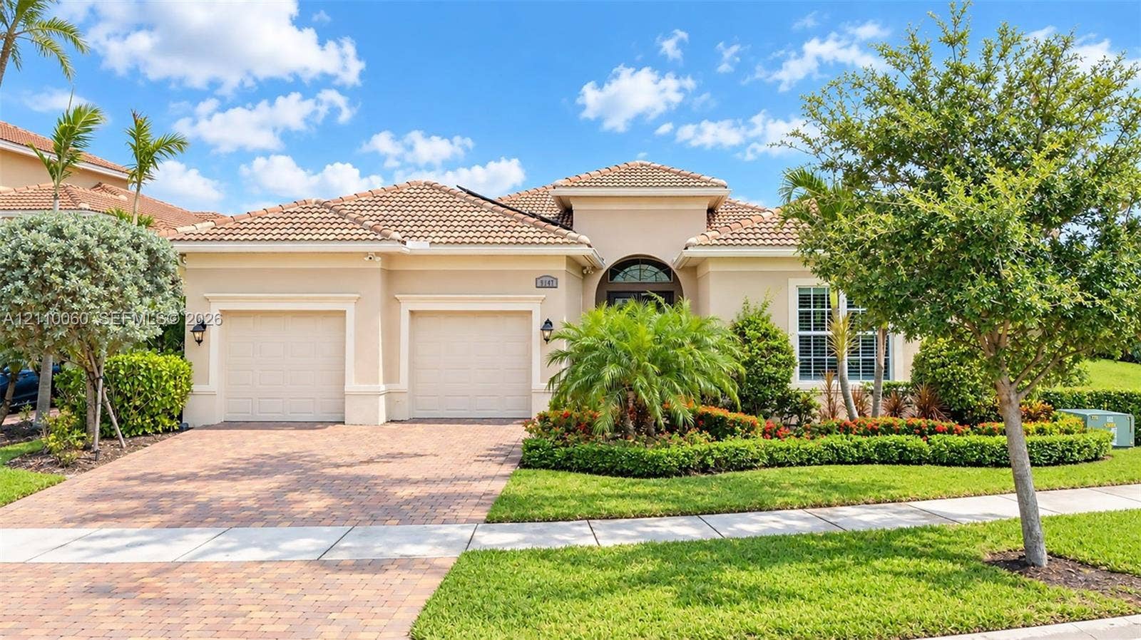 Stucco exterior featuring a multi-hipped tile roof, a two-car garage, and a paver driveway, complemented by professional landscaping