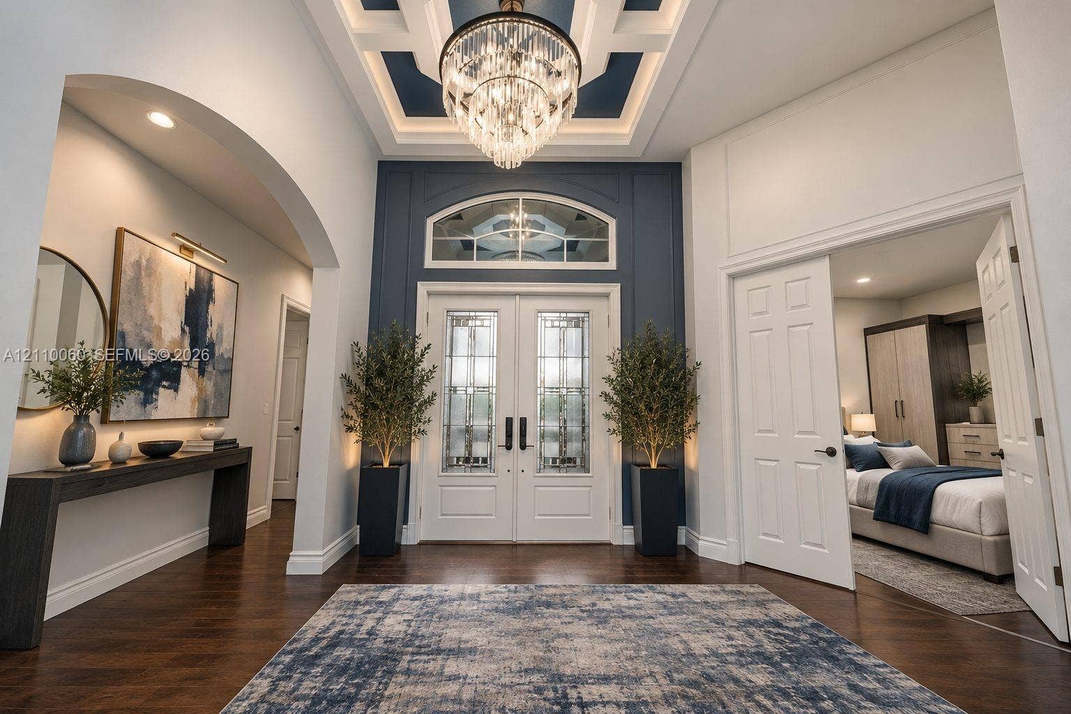 Virtually staged. Foyer featuring wood-finish flooring, a coffered ceiling with a crystal chandelier, arched entryway, and double entry doors with decorative glass inserts