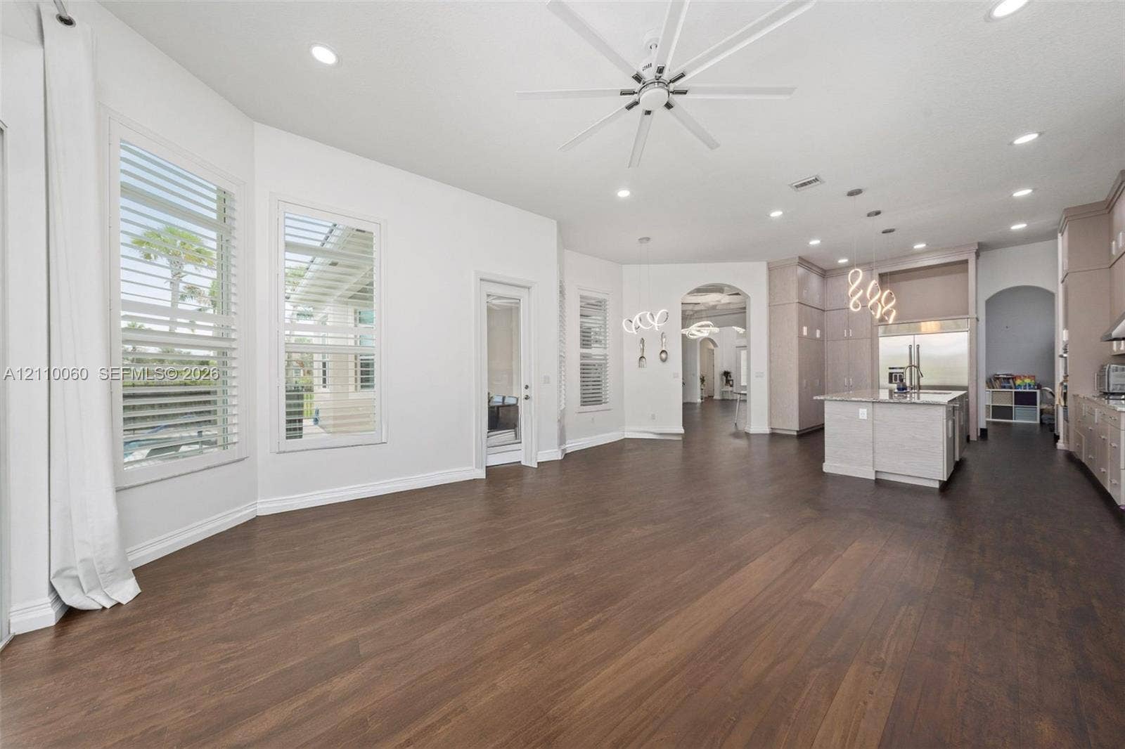 Open floor plan featuring wood-finish flooring, multi-pane windows with plantation shutters, an expansive kitchen island with a neutral countertop, recessed lighting, and an overhead ceiling fan