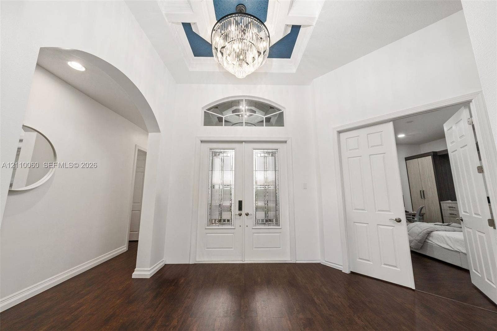 Foyer featuring double entry doors with decorative glass inserts, a recessed tray ceiling with accent color, a crystal chandelier, arched architectural detailing, and wood-finish flooring