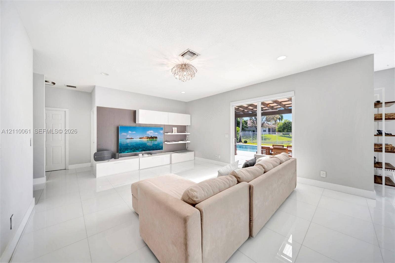 4424 E Whitewater Avenue, Weston, FL 33332 Open-concept living space featuring high-gloss tile flooring, recessed lighting, built-in media cabinetry with floating shelving, and sliding glass doors with access to a covered patio