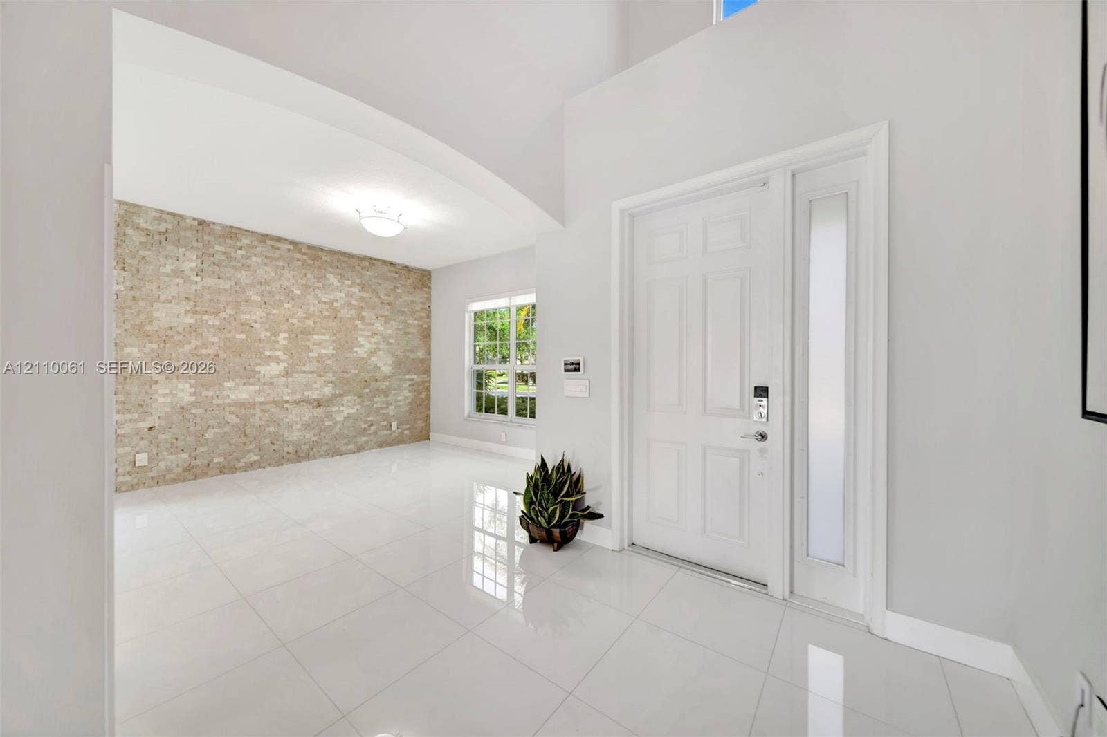 4424 E Whitewater Avenue, Weston, FL 33332 Foyer featuring high ceilings, large-format tile flooring, a prominent textured brick accent wall, and a solid-core entry door with a frosted glass sidelight