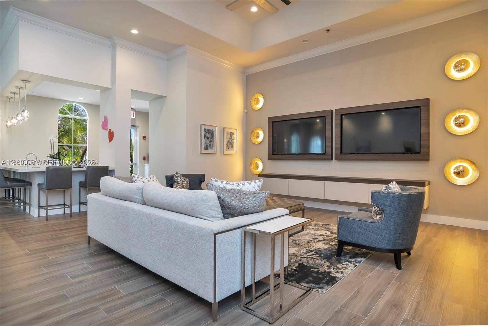 4424 E Whitewater Avenue, Weston, FL 33332 Open-concept living space featuring high tray ceilings, wood-finish flooring, a wall-mounted media console with built-in cabinetry, custom circular wall sconces, and a breakfast bar with pendant lighting