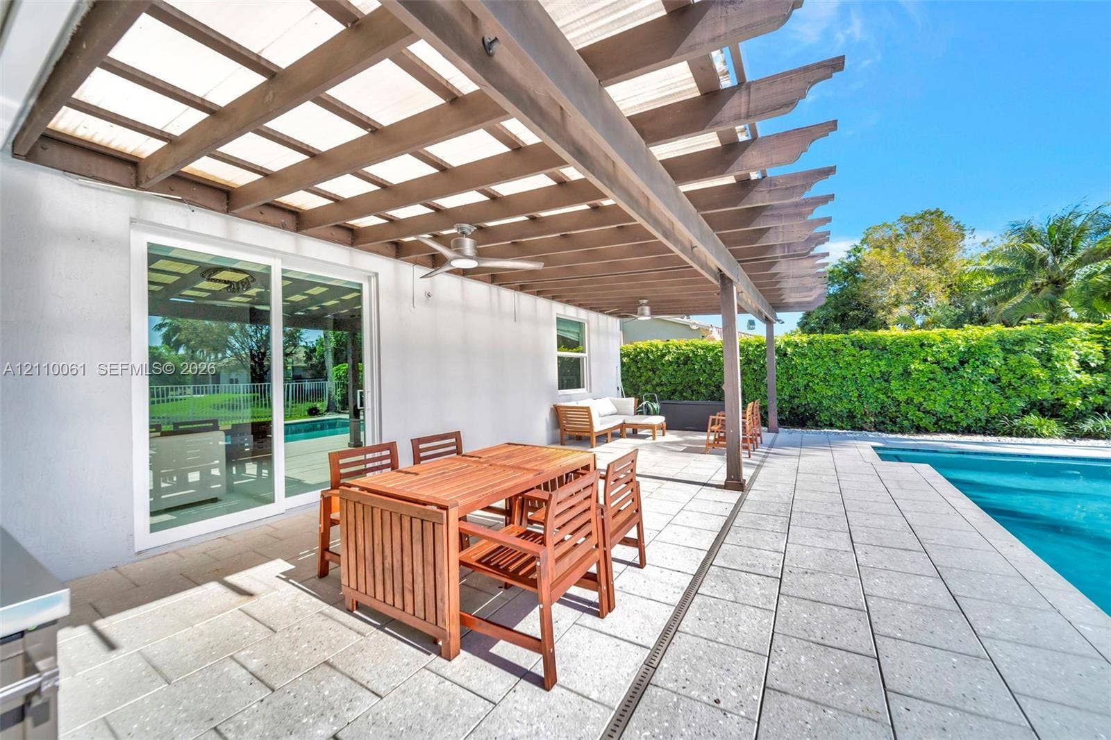 4424 E Whitewater Avenue, Weston, FL 33332 Covered patio featuring a timber pergola, built-in ceiling fans, stone paver flooring, and a swimming pool with a perimeter hedge