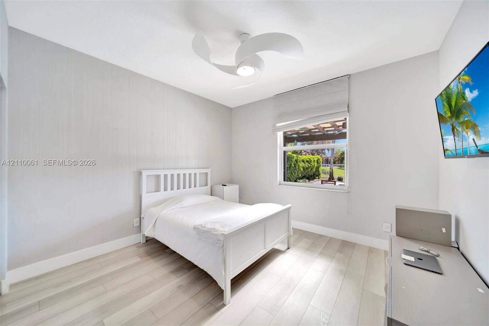 4424 E Whitewater Avenue, Weston, FL 33332 Wood-finish flooring, modern three-blade ceiling fan with integrated lighting, and neutral wall tones complemented by a window featuring a Roman shade