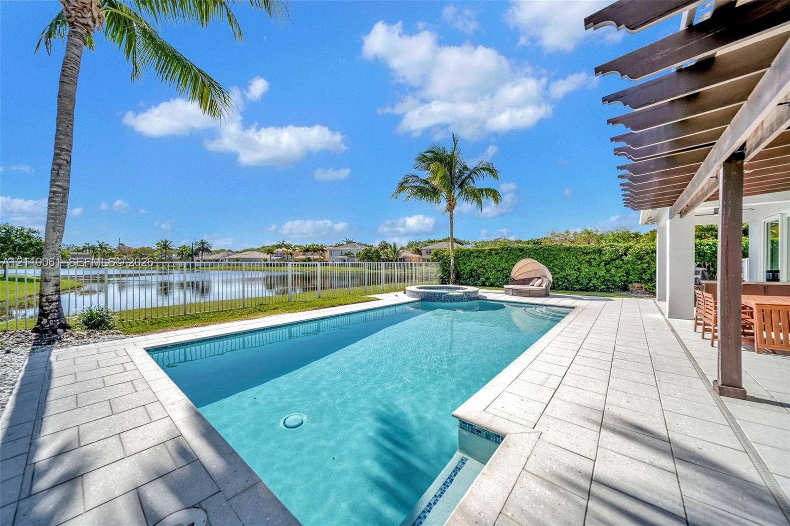 4424 E Whitewater Avenue, Weston, FL 33332 Screened pool area featuring an integrated spa, stone-tile decking, a wooden pergola, and metal perimeter fencing