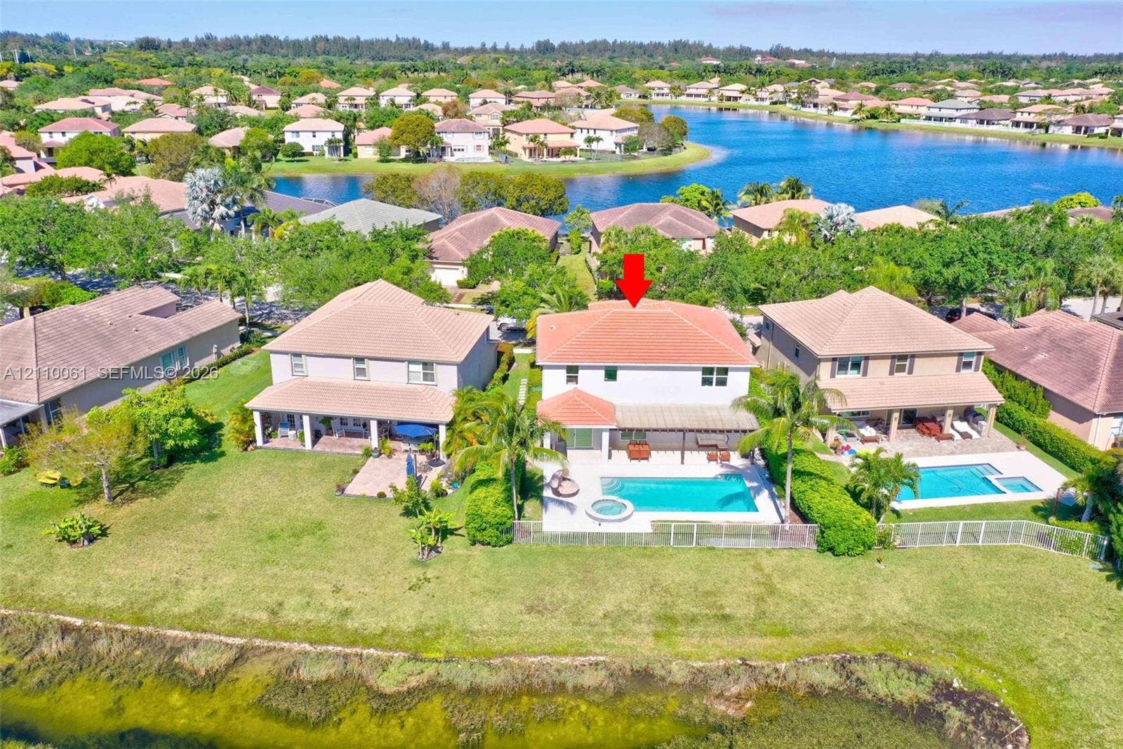4424 E Whitewater Avenue, Weston, FL 33332 Waterfront residence featuring a two-story architectural design with a terracotta tile roof, expansive manicured lawn, mature landscaping, in-ground swimming pool with surrounding hardscaping, and direct waterfront access overlooking the lake community