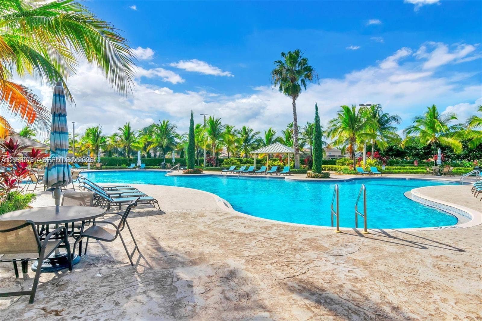 4424 E Whitewater Avenue, Weston, FL 33332 Resort-style swimming pool featuring a sprawling stone-paved deck, integrated metal ladders, shaded pavilion, and lush palm tree landscaping