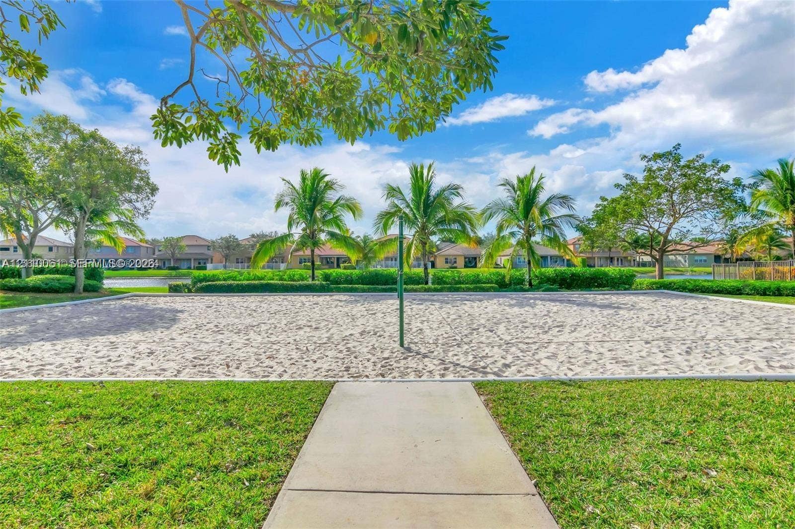 4424 E Whitewater Avenue, Weston, FL 33332 Sand volleyball court featuring a concrete walkway, perimeter landscaping, and mature palm trees
