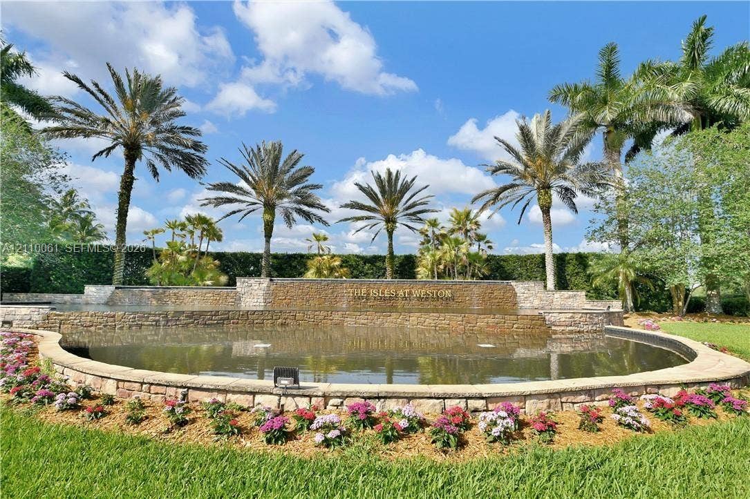 4424 E Whitewater Avenue, Weston, FL 33332 Stone-accented water feature, curated perimeter landscaping, mature palm trees, manicured turf, and tiered stone masonry walls