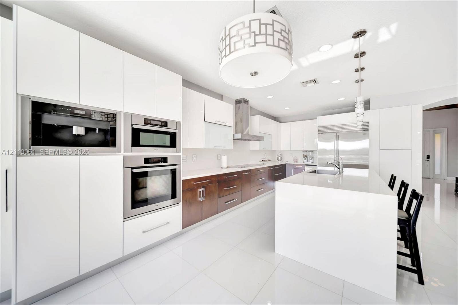 4424 E Whitewater Avenue, Weston, FL 33332 Kitchen featuring two-tone flat-panel cabinetry, a central waterfall-edge island, stainless steel built-in double wall ovens, a coordinating microwave, and a geometric-patterned drum pendant light