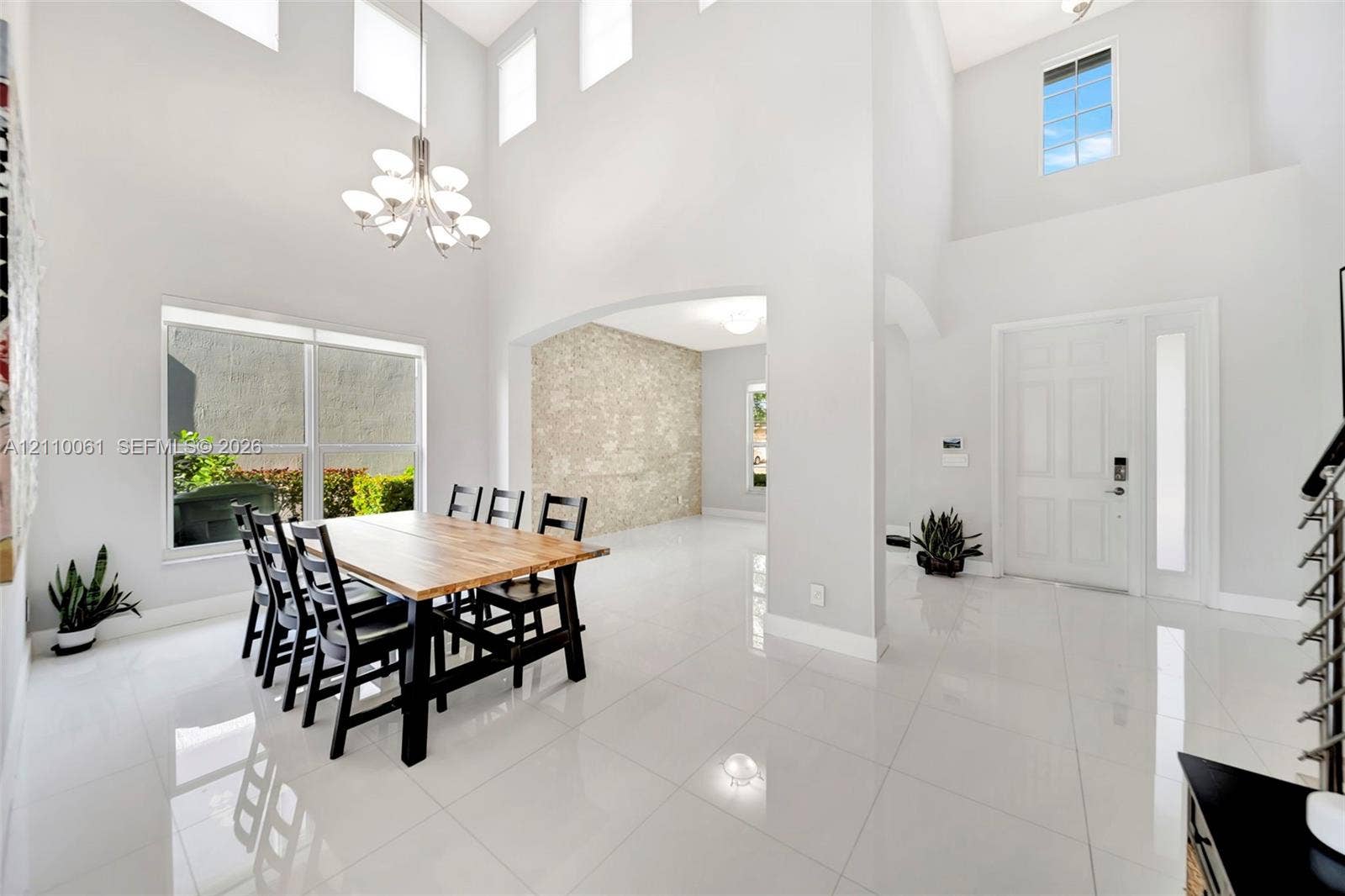 4424 E Whitewater Avenue, Weston, FL 33332 Double-height ceiling, polished tile flooring, multi-tier chandelier, stone-texture wall feature, and large windows with integrated transom lighting