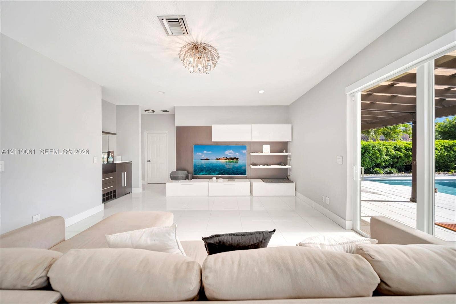 4424 E Whitewater Avenue, Weston, FL 33332 Large-format tile flooring, built-in media cabinetry with shelving, recessed lighting, and sliding glass doors leading to a covered patio with an outdoor pool
