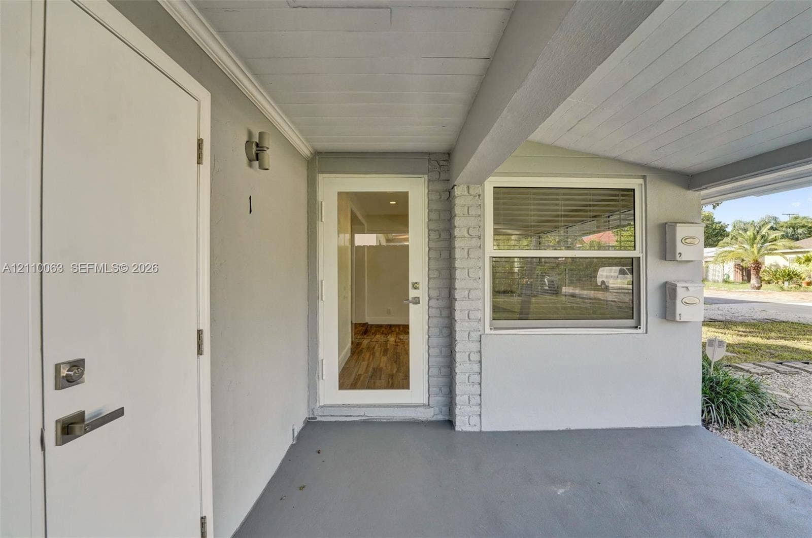 Covered entryway featuring a glass-panel entry door, brick exterior accents, dual wall-mounted mailboxes, and an external light fixture