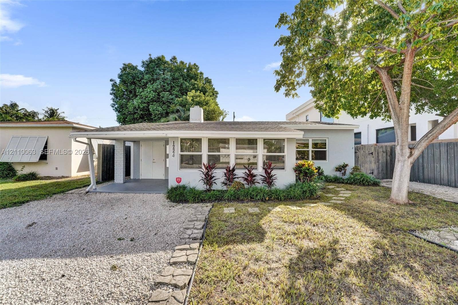 Single-story residence featuring a low-slope roof, light-colored stucco exterior, covered entryway, and stone paver accents throughout the landscaped yard