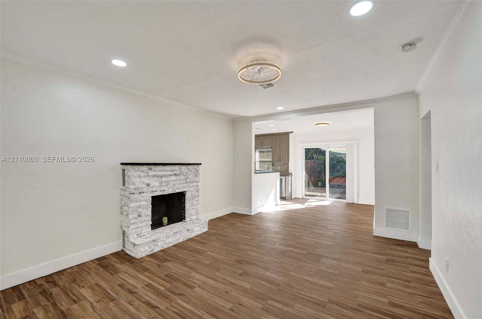 Wood-finish flooring, white stone-surround fireplace, recessed lighting, ceiling flush-mount fixture, and sliding glass door