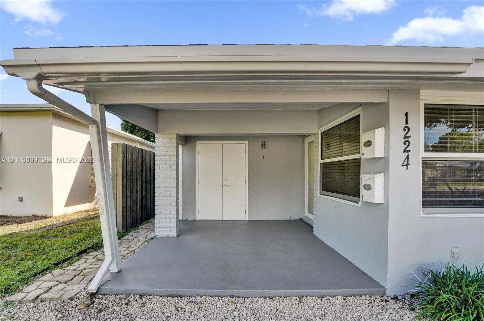 Covered entryway featuring a smooth concrete porch, white double-entry doors, painted brick accent column, and wall-mounted metal mailboxes