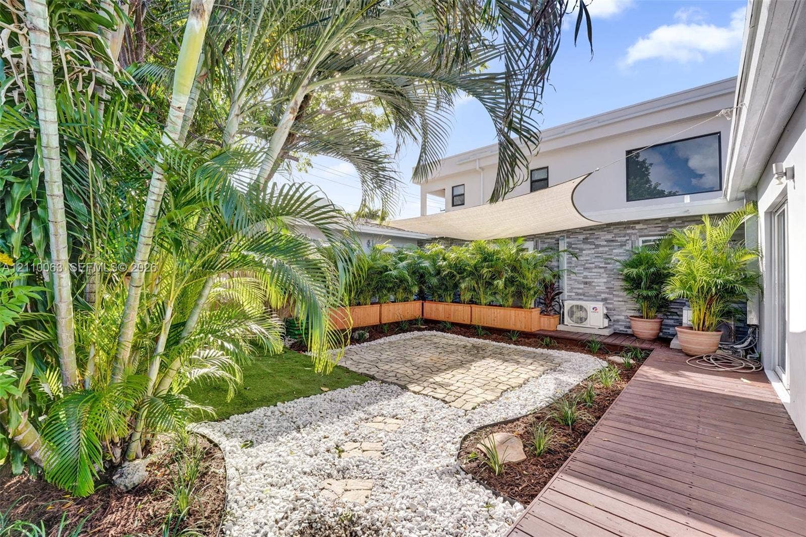 Outdoor space featuring a wood-plank deck, stone paver patio area, decorative gravel landscaping, and stacked stone exterior siding